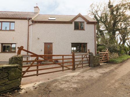 A two-story house with a wooden front door and windows behind wooden gates on a dirt road