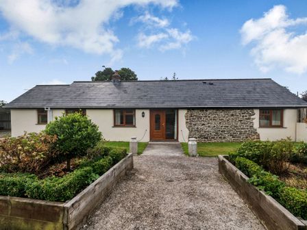 A single story house with a wooden door stone wall section and garden beds at Warbrook in Bradworthy