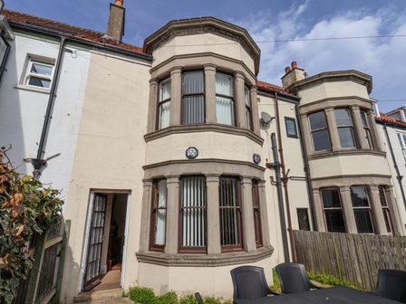 An exterior view of a house with a bay window and an open door next to a wooden fence and outdoor chairs at Mayfield Manor in Whitby