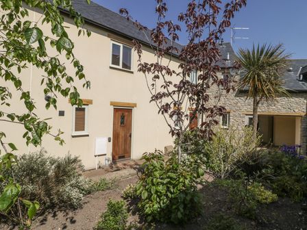 A garden with various plants and trees outside a house with a cream wall and wooden doors at 6 Malthouse Court Watchet