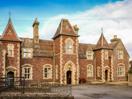 The exterior of a large stone house with multiple peaked roofs and chimneys at 3 Old Police Station in Dunster