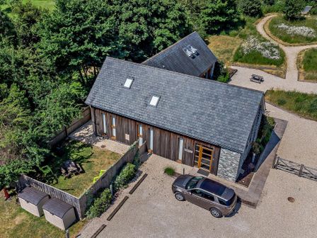 An aerial view of a building with a gravel driveway a parked car a fenced garden area and pathways surrounded by trees at Casterbridge Upwey near Weymouth