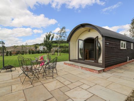 A curved wooden cabin with open double doors and a patio set with chairs on a stone patio
