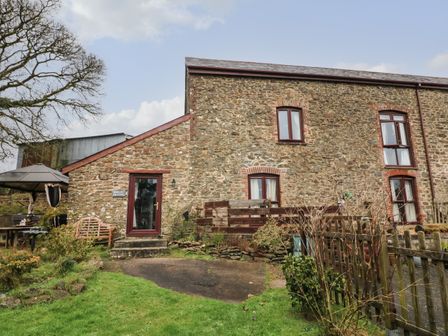 Stone house with multiple windows and a wooden door in a garden with outdoor furniture and a wooden fence at Barley Meadow in Boasley Cross near Okehampton
