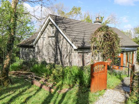 A stone cottage with a tiled roof and wooden gate surrounded by greenery at Dun na Ron in Oughterard County Galway