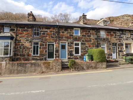 Stone terraced houses with different colored doors and windows along a roadside with bushes at Nantmel in Beddgelert