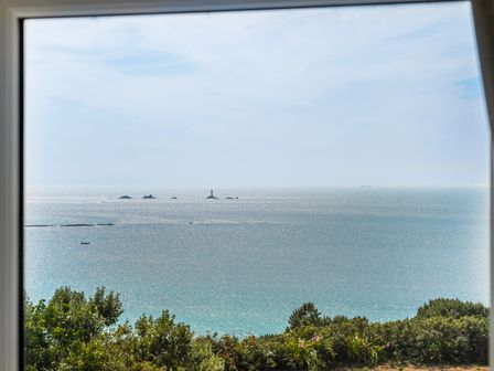 A view of the ocean from a window with a lighthouse at The Lookout in Sennen