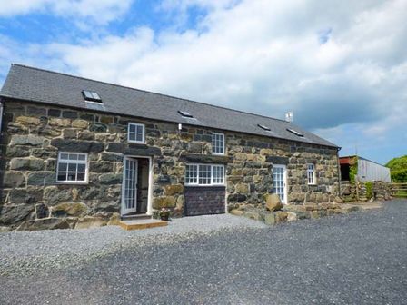 Exterior of a stone house with multiple white framed windows and doors on a gravel driveway at Y Stabal in Criccieth