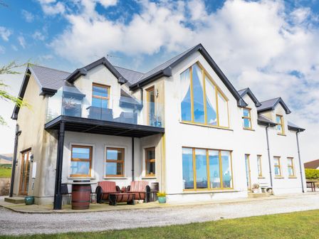 A two story house with large windows and a balcony with glass railing at Millers Lane House in Muff County Donegal