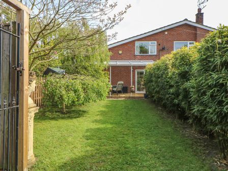 A garden with green grass and tall bushes next to a brick house with a patio at End Retreat in Wroxham