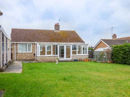 A house with a glass veranda and a green lawn in the backyard at Skylark in Weybourne