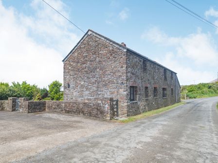 A stone barn building beside a rural road with a stone wall and gate at Penbarden Barn in Dizzard near Crackington Haven