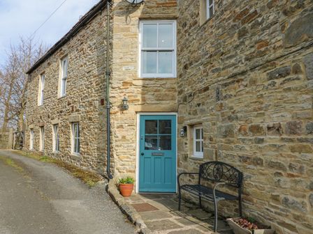 A stone building with a blue door and black bench outside at The Dale Cottage in Allendale near Hexham