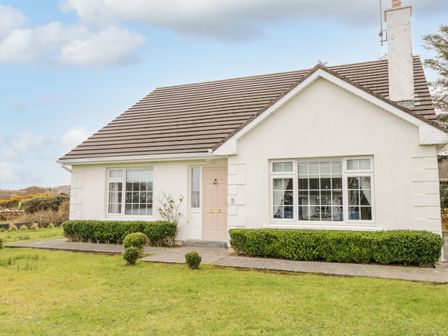 A single story house with a tiled roof and front lawn with trimmed bushes at Springwood Cottage in Louisburgh County Mayo