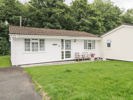 A single story house with white walls and brown tiled roof with two chairs and potted plants outside Sycamores Rosecraddoc Lodge near Liskeard
