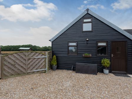 A black wooden building with windows door potted plants and wooden gate on a gravel ground at The Nook in Louth