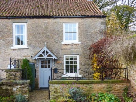A stone cottage with a tiled roof a blue door with a small porch and white framed windows at Woodside Cottage in Brompton by Sawdon
