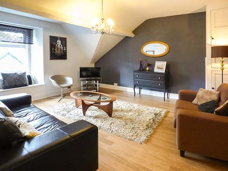 A living room with a black sofa a brown sofa a glass coffee table a TV on a stand and a chest of drawers with a mirror at High Ridge in Ambleside