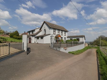 A white two story house with a tiled roof and gated driveway beside a country road at Moors Farm in Littledean