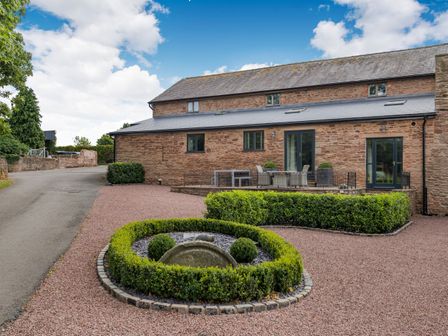 A stone building with a slate roof and outdoor seating area with hedges and stone pathway at Teal Barn Annexe in St Weonards