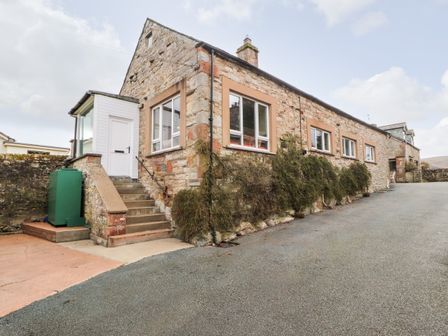 Stone building with stairs leading to a white door and multiple windows at Barnstead in Pooley Bridge