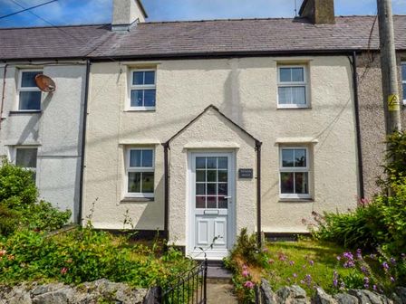 A front view of a terraced house with a white door and garden at Bwthyn Megan in Llangaffo near Newborough