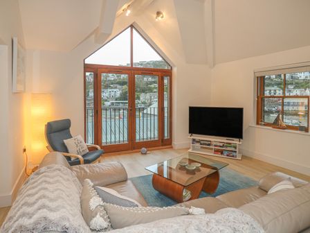 A living room with beige sofa a glass coffee table a blue armchair and a television at The Creekside in Looe