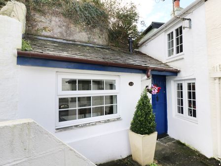 The exterior of a white house with a blue door a window a potted plant and hanging flowers at 13 Castle Hill in Lostwithiel