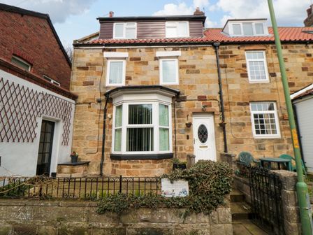 A stone house with a white door and bay window with a small front garden and a black fence at Florence Cottage in Hinderwell