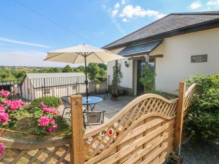 A patio area with table umbrella chairs and flowers outside a cottage at Jacks Nest in Ash Mill near South Molton