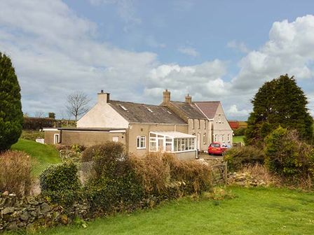 Exterior view of a countryside cottage with a garden and a parked red car at Simdda Wen Cottage in Llanddona near Beaumaris