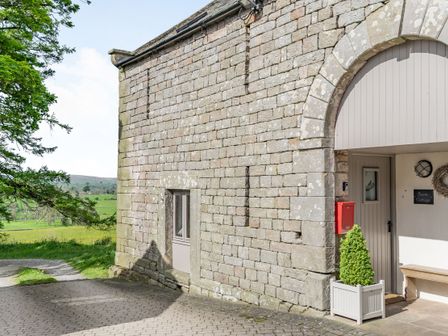 Stone cottage exterior with an arched entrance a gray door red mailbox potted shrub and a bench at Berts Cottage Heights near Appleby-in-Westmorland