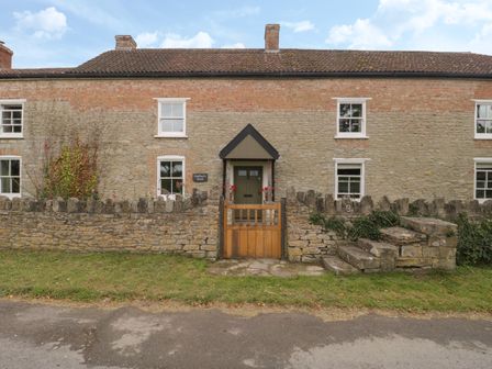 A stone and brick house with a small wooden gate and stone wall in front at Drover's in Sutton Mallet