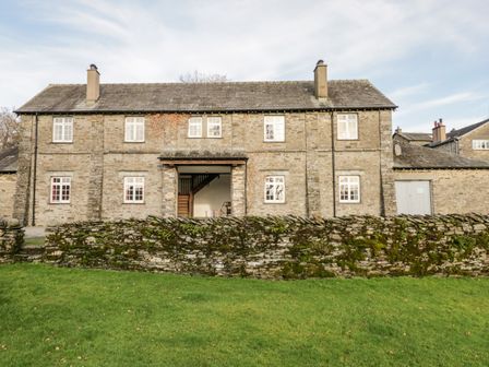 A stone house with white framed windows and two chimneys behind a mossy stone wall and green grass at Thirlmere in Sawrey near Hawkeshead