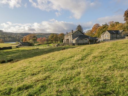 A grassy hillside with stone houses and trees in the background at Coniston Sawrey near Hawkeshead