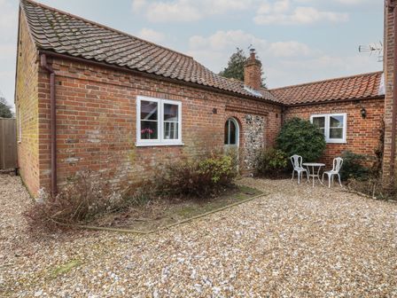 A gravel courtyard with a small white table and two chairs outside a brick building at The Annexe Fulmodestone near Fakenham