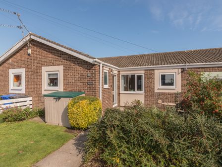 Exterior of a brick house with windows shrubs and a garden shed at Rock Rose in Beadnell