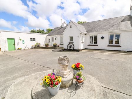 A white bungalow with a small courtyard featuring flower pots and a green door at Whispering Willows - The Bungalow in Carndonagh County Donegal
