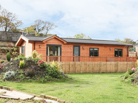 A single story wooden cabin with a fenced garden and flower beds at Thorntree Lodge in Rowsley