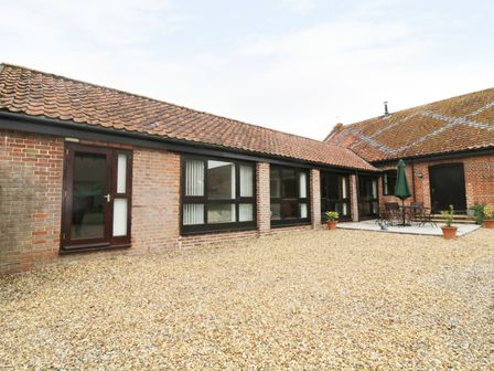 A brick exterior with tiled roof and gravel ground in a courtyard with outdoor table chairs and plants at Jackos Barn in Homersfield
