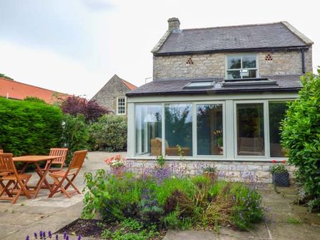A garden with wooden table and chairs and plants in front of a stone house with large windows at The Granary in Appleton-le-Moors