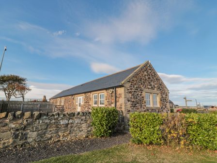A stone cottage with windows and a slate roof surrounded by a stone wall and bushes at Long Cart Cottage in Embleton