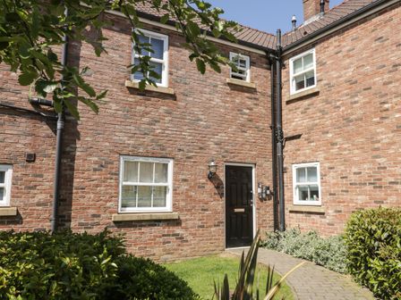 A brick house exterior with white framed windows a black door and a garden path at White Rose Apartment in Filey