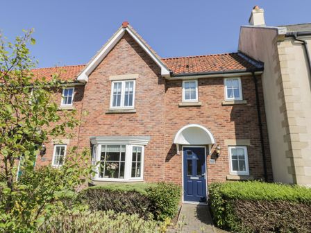 A brick house with a blue door and a bay window with bushes in front at White Rose Cottage The Bay near Filey