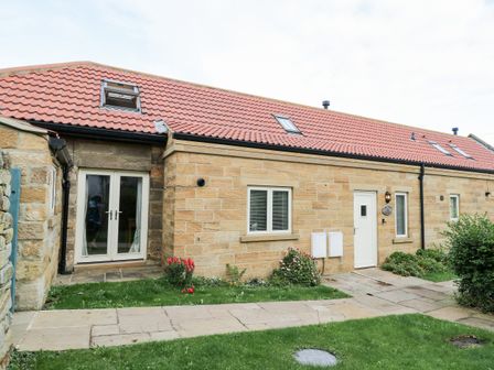 The exterior of a stone house with a tiled roof a grass lawn and a paved path at Kingfisher in Whitby