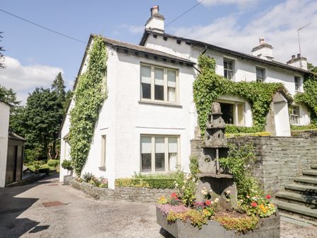 A white house with ivy on the walls and a stone planter with flowers in front at Gable End in Coniston near Hawkshead