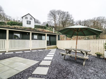 A backyard with a picnic table and umbrella on gravel and stepping stones leading to a dark building with windows at Y Felin - Celyn in Borth