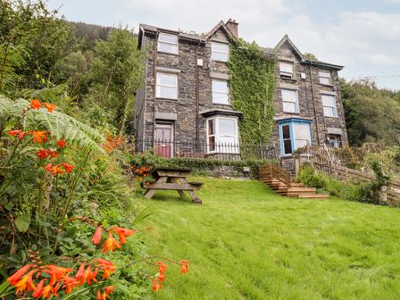 A stone house with ivy on the wall and a garden with flowers and a picnic table at 2 Isygraig in Corris