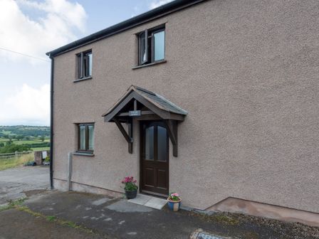 The exterior of a two-story building with a brown door under a small roof and potted plants near the entrance at Ystabl Stable in Betws Yn Rhos