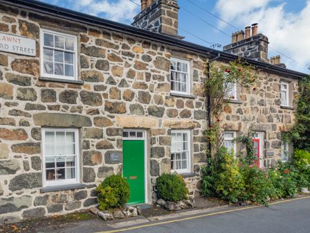 Stone cottages with white framed windows green and red doors and plants on a street at Bro Dawel in Dolgellau
